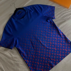 Louis Vuitton Gardient monogram T-shirt  - Snygg blå t-shirt med rött monogrammönster från Louis Vuitton. Perfekt för dig som vill sticka ut med stil. T-shirten har en klassisk passform och korta ärmar. Medföljer den klassiska orangea Louis Vuitton boxen till T-shirten! 