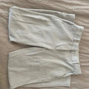 Grå rutig kostymbyxa - Snygga grå kostymbyxor med ett diskret rutmönster från H&M. Byxorna har en klassisk passform med hällor för bälte och stängs med dragkedja och hyska. Perfekta för en stilren look.