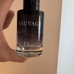 Sauvage parfym från Dior - Säljer en elegant flaska av Sauvage parfym från Dior. Flaskan har en stilren design med en mörk toning som övergår till klar vid botten. Perfekt för den som söker en sofistikerad doftupplevelse. Det är 25-30 ml kvar 