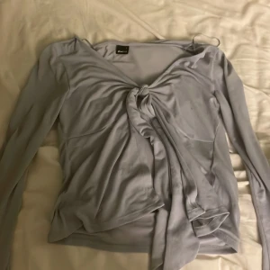 Ljusblå långärmad topp från Gina Tricot - Säljer en ljusblå långärmad topp från Gina Tricot med knytning framtill. Toppen har en v-ringad design och är tillverkad i ett mjukt material. Perfekt för en stilren look.