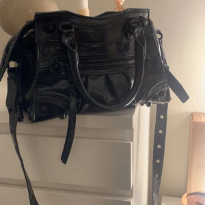 Svart handväska med dragkedja från Steve Madden  - Snygg svart handväska i skinn med dragkedja och justerbar axelrem. Perfekt för att bära dina dagliga nödvändigheter med stil. Väskan har flera fack och en cool design som passar till många olika outfits. Nytt pris 1 345kr. Är villig att diskutera pris.