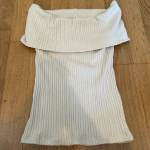 Vit ribbad offshoulder topp - Säljer en stilren beige ribbad offshoulder topp. Perfekt för en trendig look med sin unika design. Passar bra till både jeans och kjol. 