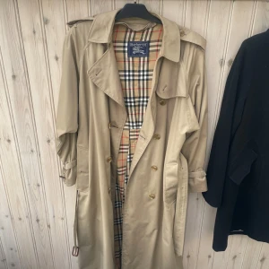 Burberry Women's Vintage Cream Beige Check Haymarket Trench Coat .  - Burberry Women's Vintage Cream Beige Check Haymarket Trench Coat .                                   Säljer en klassisk beige trenchcoat från Burberry i mycket bra skick. Den har det ikoniska rutiga fodret och knappar framtill. Perfekt för höst och vår, med en tidlös stil som funkar till allt. Passar både till vardags och lite finare tillfällen. 🧥✨Ny pris på denna och burberry kappor i den här stilen ligger mellan 20-25 000kr