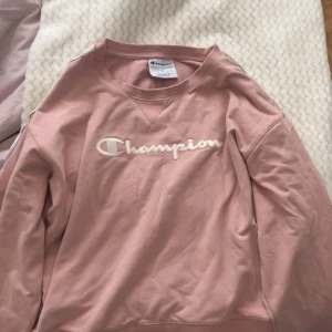 Rosa sweatshirt från Champion - Säljer en rosa sweatshirt från Champion med deras ikoniska logga broderad på framsidan. Tröjan har långa ärmar och ribbade muddar vid ärmslut och nederkant. 💗skulle även vilja påpeka att den sitter mer som en storlek S än L. 