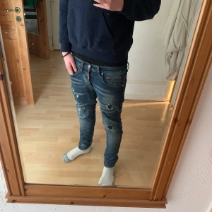 Jeans från dsquared2 - Säljer ett par snygga blå jeansbyxor från dsquared2 med coola slitningar på framsidan. De har en klassisk femficksdesign och en läderpatch på baksidan. Perfekta för en avslappnad stil.