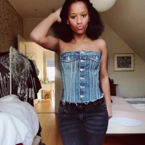 Jeanskorsett med knappar - Snygg jeanskorsett med knappar framtill och en tight passform. Perfekt för att ge en cool och trendig look. Axelbandslös design som framhäver axlarna. DEN HAR TVÅ HÅL DÄR BAK men det är ingenting som påverkar toppen alls, syns knappt