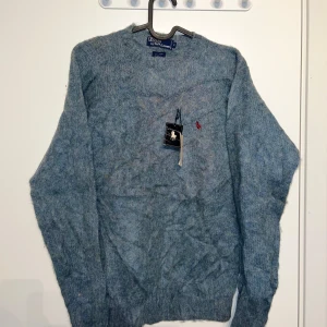 Blå stickad tröja från Polo Ralph Lauren - Säljer en snygg blå stickad tröja från Polo Ralph Lauren med det klassiska röda logotypbroderiet på bröstet. Tröjan har en normal passform och långa ärmar, perfekt för kyligare dagar. Ett måste för garderoben! 💙