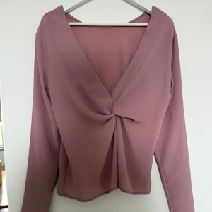 Rosa långärmad topp från NLY Trend - Säljer en stilren rosa topp från NLY Trend med lång ärm och v-ringning. Toppen har en snygg knutdetalj baktill som även kan användas åt andra håller så knuten hamnar framtill. Storlek 38.