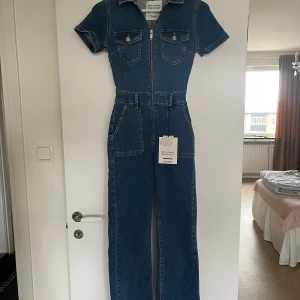 Jeans jumpsuit från Pull&Bear storlek S - Snygg jeans jumpsuit från Pull&Bear med korta ärmar och dragkedja framtill. Den har två bröstfickor med knappar och två stora fickor på sidorna. Perfekt för en avslappnad stil med en touch av denim. Avklippta ben. Passar mig perfekt som är 160cm. Aldrig använd!! 