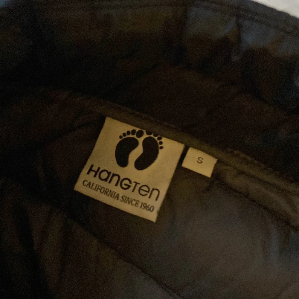 Snygg svart dunväst från Hang Ten med dragkedja framtill. Perfekt för lager-på-lager under kyligare dagar. Västen har en stilren design med quiltade paneler.. Takit.