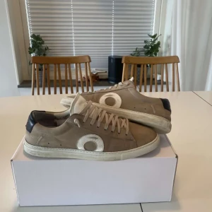 Beige sneakers från Oliver Cabell - Snygga beige sneakers från Oliver Cabell med vita detaljer och snörning. Skorna har en rund tå och en diskret design som passar perfekt till vardags. De är tillverkade i ett stilrent material med en kontrasterande svart häl. Det är 29,5 cm innermått. Skriv vid funderingar 🌟