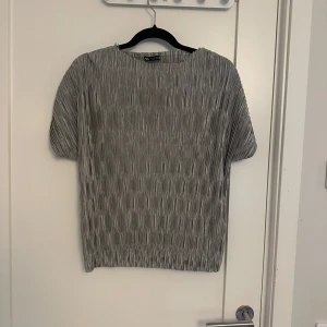 Grå kortärmad topp från Zara - Säljer en stilren grå topp från Zara med korta ärmar och ett veckat mönster. Perfekt för en chic och avslappnad look. Passar bra till både jeans och kjol.