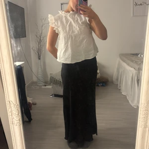 Vit blus med volangdetaljer - Säljer en söt vit blus med volangdetaljer vid ärmarna och halsen. Blusen har en luftig passform och är perfekt för varmare dagar. Den är ärmlös och ger en romantisk touch till din outfit.( nytvättad och inte strykt den(