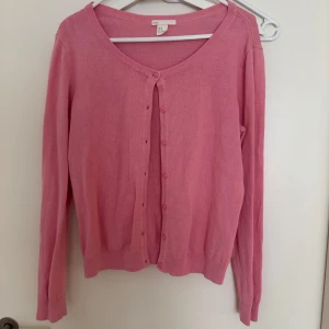 Rosa kofta från Basic HM - Säljer en söt rosa kofta från Basic med knappar framtill. Koftan har en rund halsringning och långa ärmar. Perfekt för att lägga till en färgklick i din garderob!