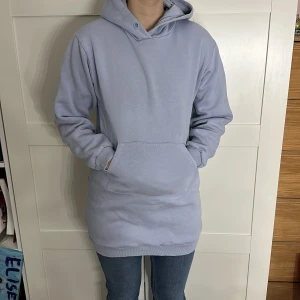 Ljusblå hoodie - Säljer en mysig ljusblå hoodie med ficka framtill. Perfekt för kyliga dagar med sin bekväma passform och långa ärmar. Huvan ger extra värme och stil.