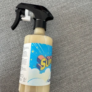 Lush Super Milk Glitter Mist - Super Milk Glitter Mist från Lush i en stor sprayflaska på 260g. Innehållet är ljusgult med skimrande glittereffekt. Perfekt för att ge huden en fräsch och glittrig finish. Flaskan har en cool, färgglad etikett med retroinspirerad design. 