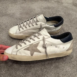 Vita sneakers med grå stjärna - Snygga vita sneakers med grå mockadetaljer och en stor grå stjärna på sidan. Skorna har grå snörning, beige sula och mörkblå häl. Perfekta för en avslappnad och trendig look.