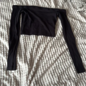 Svart offshoulder topp från Bik Bok - Säljer en svart, ribbad offshoulder topp från Bik Bok i storlek XS. Toppen är croppad med långa ärmar och har en tight passform som sitter snyggt över axlarna. Perfekt för dig som gillar stilrena och trendiga plagg.