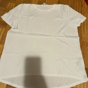 Vit t-shirt från Amisu i XL - En clean vit t-shirt från Amisu i storlek XL. Modellen har rund halsringning och korta ärmar, med en något längre baksida för en chill look. Tillverkad i mjuk bomull som känns skön mot huden. Perfekt för dig som gillar enkel och stilren vibe.