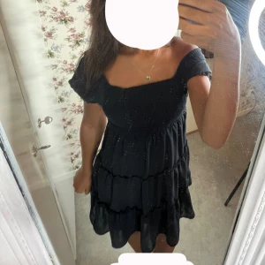 Svart kort klänning med puffärm - Supersöt svart klänning från Cubus med puffiga korta ärmar och smock upptill. Klänningen har volanger i kjolen och en fyrkantig urringning. Perfekt för dig som gillar en feminin och trendig look. Materialet är lätt och luftigt.