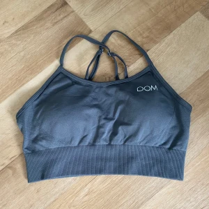 Grå sporttopp från Drop of Mindfulness - Snygg grå sporttopp från Drop of Mindfulness med smala axelband som korsas i ryggen. Toppen har en ribbad nederkant och är tillverkad i ett stretchigt material som passar perfekt för träning. Diskret logga framtill och textdetalj bak.