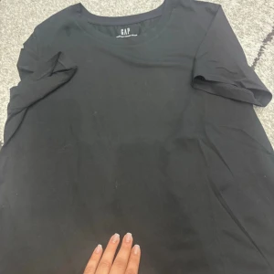 Svart basic t-shirt från GAP - En klassisk svart t-shirt från GAP med rund hals och korta ärmar. Enkel och stilren modell i mjuk bomull, perfekt till jeans eller shorts. Passar dig som gillar en clean och tidlös look.