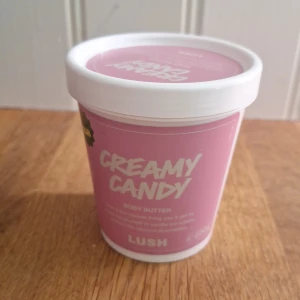 Lush Creamy Candy Body Butter 230g - Creamy Candy Body Butter från Lush i en söt rosa och vit plastburk, 230g. Innehåller bland annat mandelolja, murumurusmör, kakaosmör och vaniljextrakt. Ger huden en mjuk och återfuktad känsla med en godisdoft. Perfekt för dig som älskar söta dofter och veganska produkter. Produkten är endast testad en gång men annars helt ny!