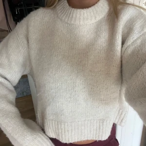 Vit stickad tröja - Mysig vit stickad tröja med croppad passform och ribbad halsringning. Perfekt för dig som gillar en enkel och clean look. Tröjan har långa ärmar och är superenkel att matcha med jeans eller kjol. Passar dig som vill ha en chill och stilren vibe.