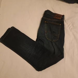 Mörkblå Lee Luke jeans W33 L34 - Säljer ett par mörkblå Lee Luke jeans i klassisk denim med snygga kontrastsömmar och läderpatch bak. Modellen har en modern passform och raka ben. Perfekta för dig som gillar stilrena och tidlösa jeans.