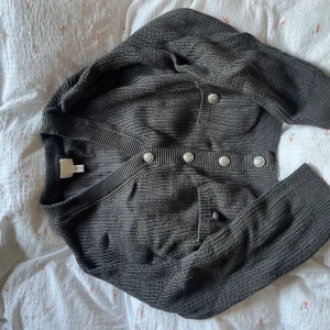 Grå stickad kofta från H&M - Säljer en grå stickad kofta från H&M i storlek S. Koftan har en loose passform, långa ärmar och snygga silvriga knappar framtill. Ribbad vid muddar och nederkant, samt två praktiska fickor. Perfekt att slänga över en t-shirt för en chill look.