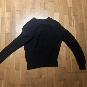 Svart stickad tröja från lager 157 - Svart stickad tröja från lager 157 i storlek S. Tröjan har en klassisk rund hals och långa ärmar. Den är ribbstickad och har en enkel, clean look som funkar till många olika stilar. Perfekt att slänga på sig när det är lite kyligt ute.