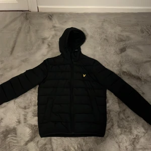 Mörkblå vinter pufferjacka från Lyle & Scott - Mörkblå vinter pufferjacka från Lyle & Scott med huva och dragkedja. Jackan har det klassiska Lyle & Scott-loggan i gult på bröstet och är tillverkad i återvunnen nylon och polyester. Perfekt för kalla dagar och har en clean, stilren look. Jackan är köpt för 1000kr på Zalando 10/10 skick inga defekter, använd fåtal gånger under en vinterperiod färgen är mörkblå men svårt att se hör av er om ni har frågor //Leo
