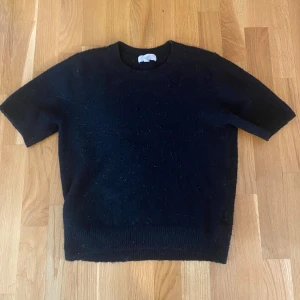 Svart stickad tröja från H&M - En svart stickad tröja från H&M i storlek XS. Tröjan har rund hals och korta ärmar, perfekt för dig som gillar enkel och stilren design. Materialet är mjukt och ger en skön känsla mot huden. Passar dig som vill ha en klassisk look med modern touch.