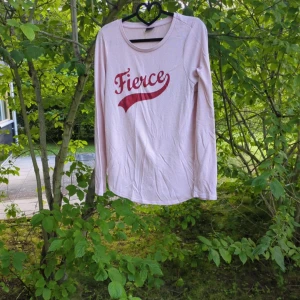 Ljusrosa långärmad tröja Fierce - Säljer en ljusrosa långärmad tröja från Gina Tricot i storlek L. Tröjan har ett coolt rött tryck med texten 'Fierce' på bröstet och är gjord i mjuk bomull. Rund halsringning och normal passform, perfekt för dig som gillar statement-plagg. Den är välanvänd men har mer att ge, noppor finns och den är en aning tvättpåverkad.  Katter finns i hemmet.