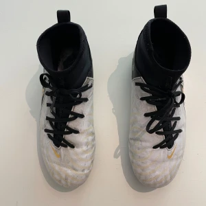 Nike Phantom Luna Academy FG/MG – Strl 38,5 – Fint skick - Snygga och stabila fotbollsskor – redo för både natur- och konstgräs! Lite använda Nike Phantom Luna Academy FG/MG i storlek 38,5. Färg: vit/svart med guld. Nypris ca 950 kr (2024). Skicket: gott och funktionsdugligt, snören och dobbar med normalt slitage.  Finns i Spånga