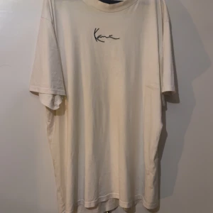 Oversized vit t-shirt från Karl Kani - Vit oversized t-shirt från Karl Kani med svart broderad logga på bröstet. Klassisk rund hals och korta ärmar. Tillverkad i mjuk bomull som känns skön mot huden. Perfekt för dig som gillar streetwear och enkel stil.