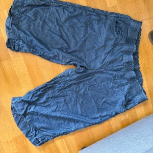 Blå loose shorts från bpc - Säljer ett par blå loose shorts från bpc bonprix collection. De har hög midja med bred, smockad resår och volangkant upptill. Materialet är mjukt och lätt, perfekt för varma dagar. Shortsens avslappnade passform gör dem riktigt sköna att bära.