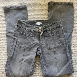 Grå bootcut jeans  - Snygga grå jeans från Gina Tricot med bootcut och två stora framfickor. Det är lågmidjade och har dubbla knappar  med markerade sömmar längs benen. Perfekta för en cool och avslappnad stil. 