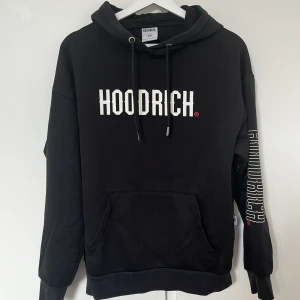 Svart HOODRICH hoodie med tryck XS - Svart hoodie från HOODRICH med stor vit logga på bröstet, tryck på ryggen och ena ärmen. Storlek xs men passar också S. Metallgrejen längst ner på ena snöret har ramlat av. 