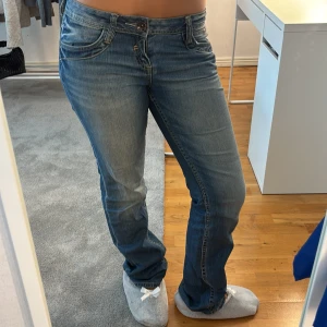 QS by s.Oliver blå jeans lågmidjade - Snygga blå jeans från QS by s.Oliver, modell Catie. De har låg midja och rakt snitt med en slim fit. Klassisk femficksdesign, ljus tvätt och subtila slitningar. Perfekta för dig som gillar en avslappnad men ändå stilren look.