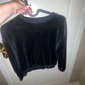 Svart sammets tröja från Kappahl - Mjuk och stilren svart tröja från Kappahl i storlek 134/140. Tröjan har rund hals, långa ärmar och är gjord i glansig sammet som ger en lyxig känsla. Perfekt för dig som gillar enkel men snygg stil.