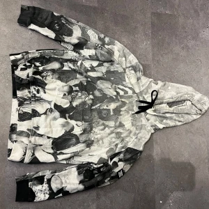 Burberry hoodie med svartvit print - Säljer en unik hoodie från Burberry med svartvit all-over print av fotomotiv. Tröjan har huva med svarta snören och klassisk känguruficka. Mjuk insida och cool streetkänsla, perfekt för dig som vill sticka ut med designerplagg.