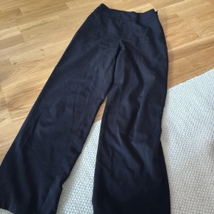 Svarta vida kostymbyxor - Snygga svarta kostymbyxor med vid passform och hög midja. Perfekta för en clean och stilren look. Byxorna har raka ben och är gjorda i ett mjukt tyg som känns skönt mot huden.