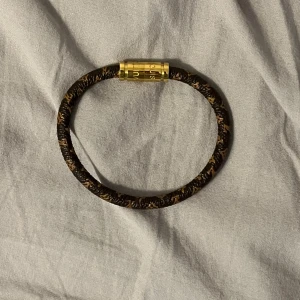 L v armband  - Brunflätat lv armband med många detaljer med ett guldigt magnetlås 