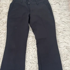 Svarta kostymbyxor med bootcut - Stilrena svarta kostymbyxor med bootcut-snitt och klassiska fickor framtill. Byxorna har hällor för bälte och är sydda i ett mjukt tyg som ger en dressad känsla. Perfekta för dig som gillar en clean och tidlös look. Jag har sprätta upp de så att de är lite längre där ner 