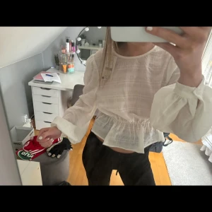 Vit blus med voluminösa ärmar - Supersöt vit blus med voluminösa långa ärmar och lätt rynkad midja. Tunt, luftigt tyg med subtilt rutigt strukturmönster och rund halsringning. Perfekt för dig som gillar en romantisk och trendig look.