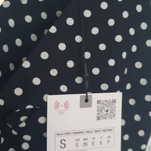 Svart prickig långklänning S - Supersnygg svart långklänning med vita prickar och slits framtill. Klänningen har korta ärmar, v-ringning och knyt i midjan för en smickrande siluett. Perfekt för dig som gillar retrovibbar och vill sticka ut med ett klassiskt mönster. Materialet känns lätt och luftigt.