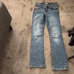 Blå bootcut jeans med fickdetaljer - Säljer ett par klassiska blå jeans med bootcut passform och snygga fickor med lock och knapp bak. Är även inte i ett så använt skick, pris kan diskuteras 