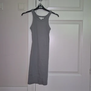 Grå ribbad ärmlös klänning H&M XS - Snygg grå ribbad klänning från H&M i storlek XS. Modellen är ärmlös med rundad hals och har en kroppsnära passform. Perfekt för dig som gillar enkel och stilren design. Materialet är mjukt och stretchigt, vilket gör den superbekväm att bära.