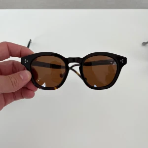 Bruna runda solglasögon - Snygga solglasögon med rundad form och bruna glas. Bågarna är mörkbruna med en klassisk look och små silvriga detaljer vid hörnen. Glasögonbox ingår. Finns fler modeller i min profil.